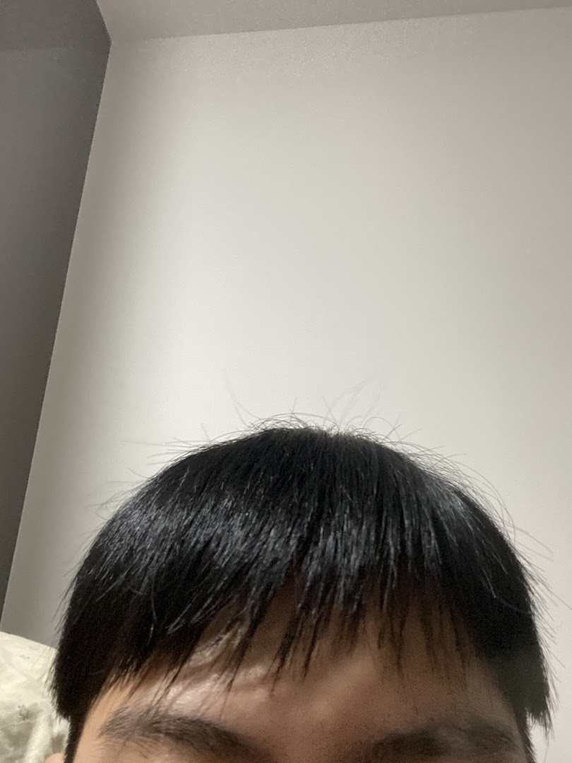 Close-up of a person's black hair and forehead, showcasing hair texture and style.