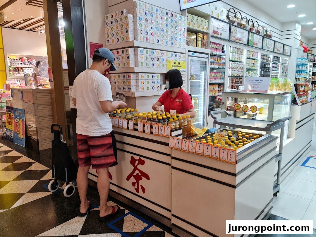 A customer interacts with staff at a counter displaying traditional tonic drinks and health products.