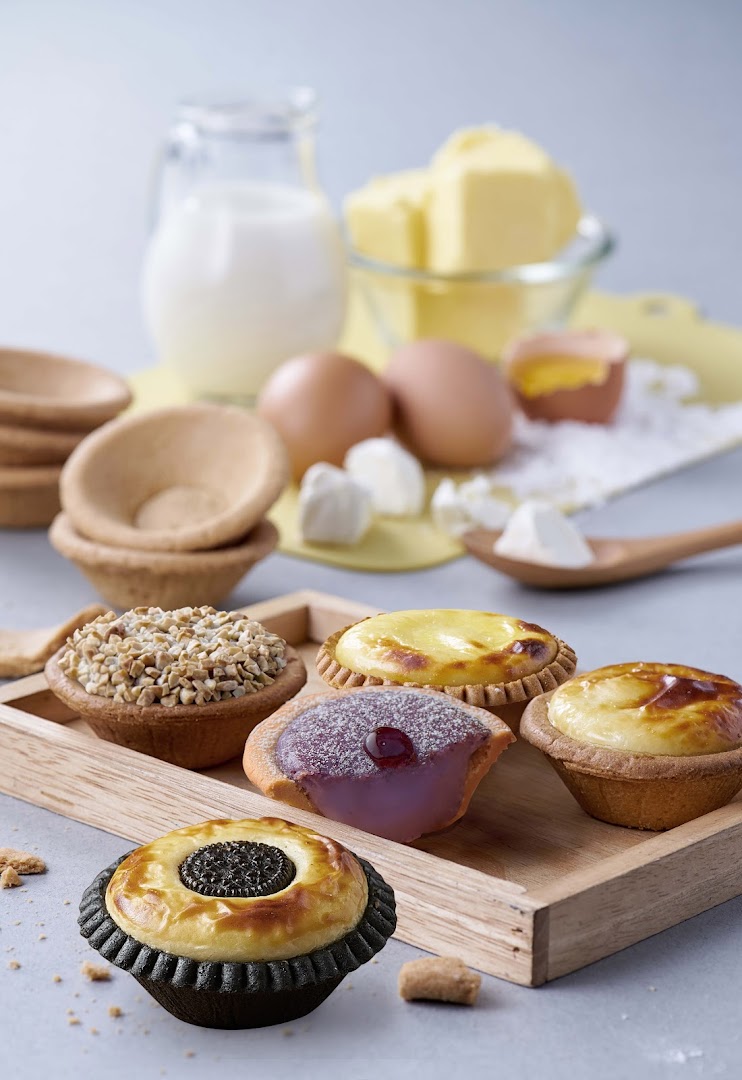 Assortment of delicious tarts with baking ingredients like milk, eggs, and butter, on a wooden tray.