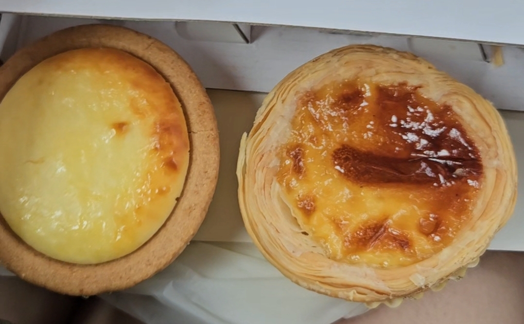 Close-up of a Hokkaido Baked Cheese Tart and a Portuguese egg tart in a box.