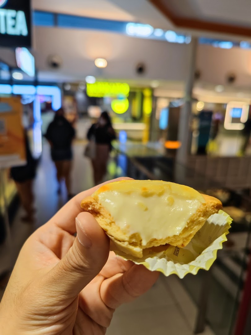 A hand holds a delicious Hokkaido Baked Cheese Tart, showcasing its creamy filling in a mall setting.
