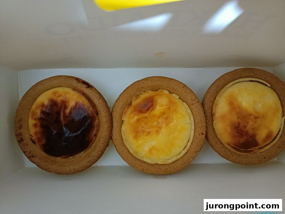 Three delicious Hokkaido Baked Cheese Tarts with golden-brown tops in a white box.