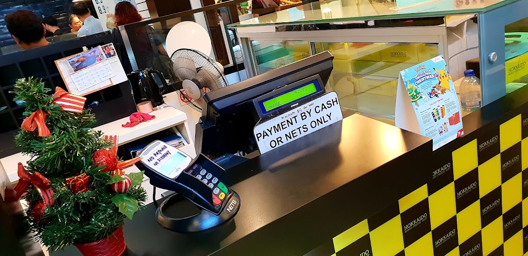A festive counter at Hokkaido Baked Cheese Tart, featuring a payment terminal, Christmas decor, and branded packaging.