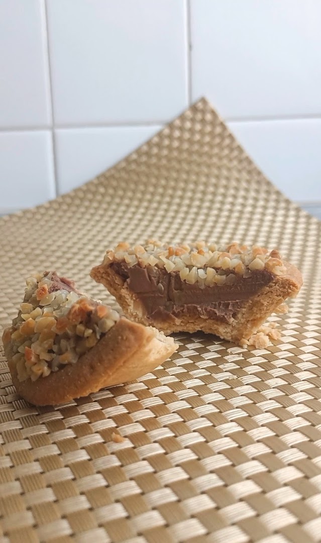 A delicious tart, cut in half, revealing a rich chocolate or caramel filling and a crunchy nut topping.