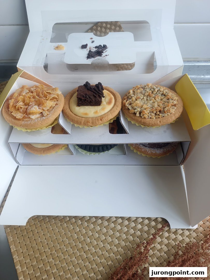 A box of assorted Hokkaido Baked Cheese Tarts with various toppings, including cornflakes, brownie, and nuts.
