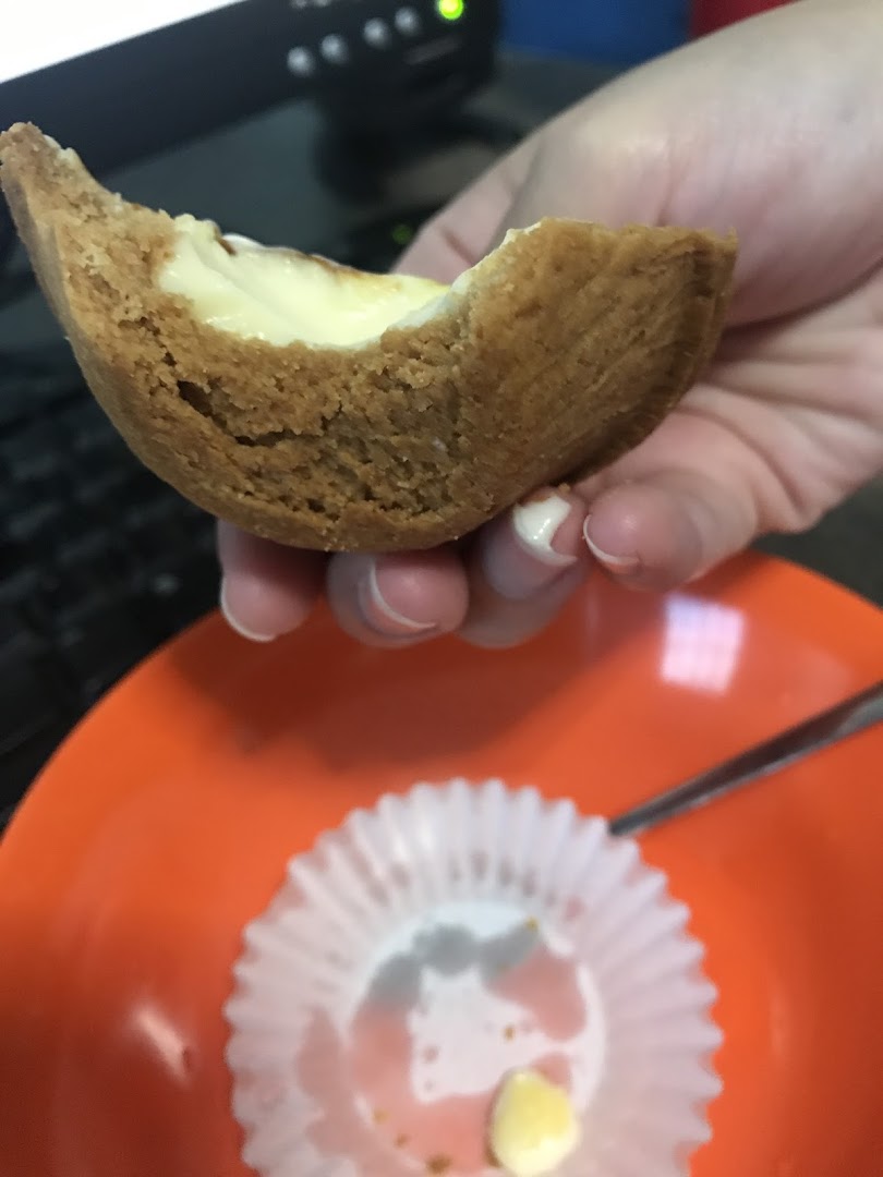 A hand holds a delicious, partially eaten Hokkaido Baked Cheese Tart over an orange plate.