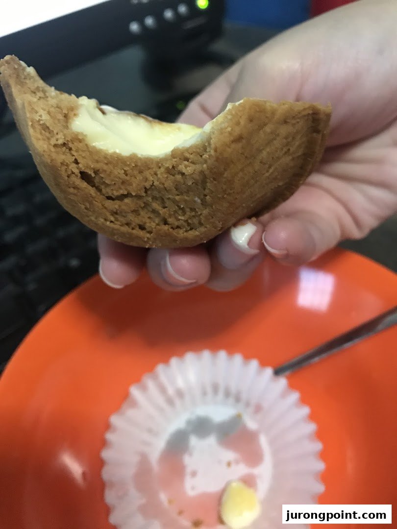 A hand holds a delicious, partially eaten Hokkaido Baked Cheese Tart over an orange plate.
