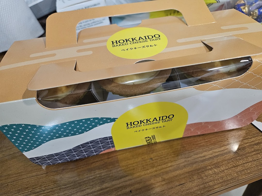 A branded box of Hokkaido Baked Cheese Tarts, showcasing the delicious pastries through a clear window.