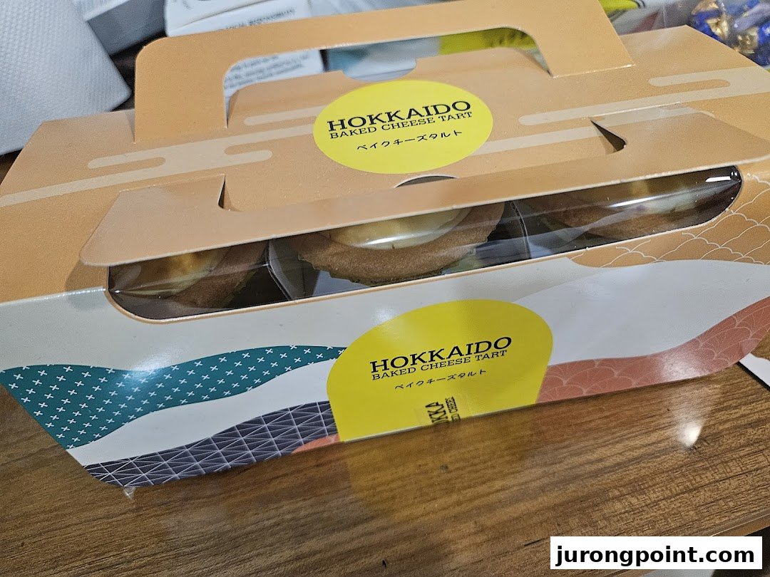 A branded box of Hokkaido Baked Cheese Tarts, showcasing the delicious pastries through a clear window.