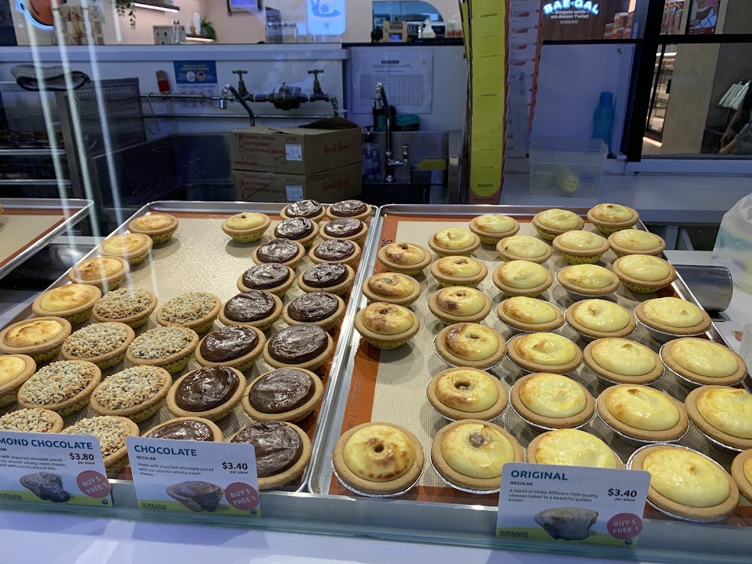 A vibrant display of Hokkaido Baked Cheese Tarts with visible pricing for various flavors.