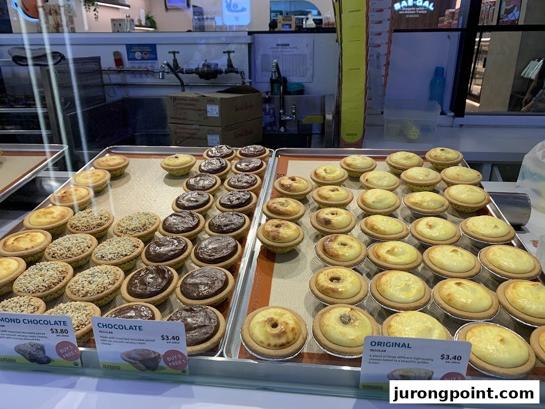 A vibrant display of Hokkaido Baked Cheese Tarts with visible pricing for various flavors.