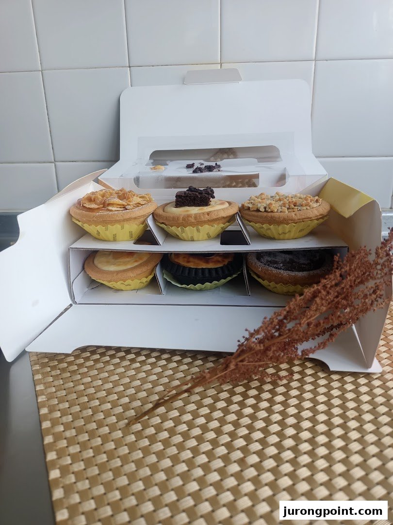 A white box containing six assorted Hokkaido Baked Cheese Tarts on a woven mat.