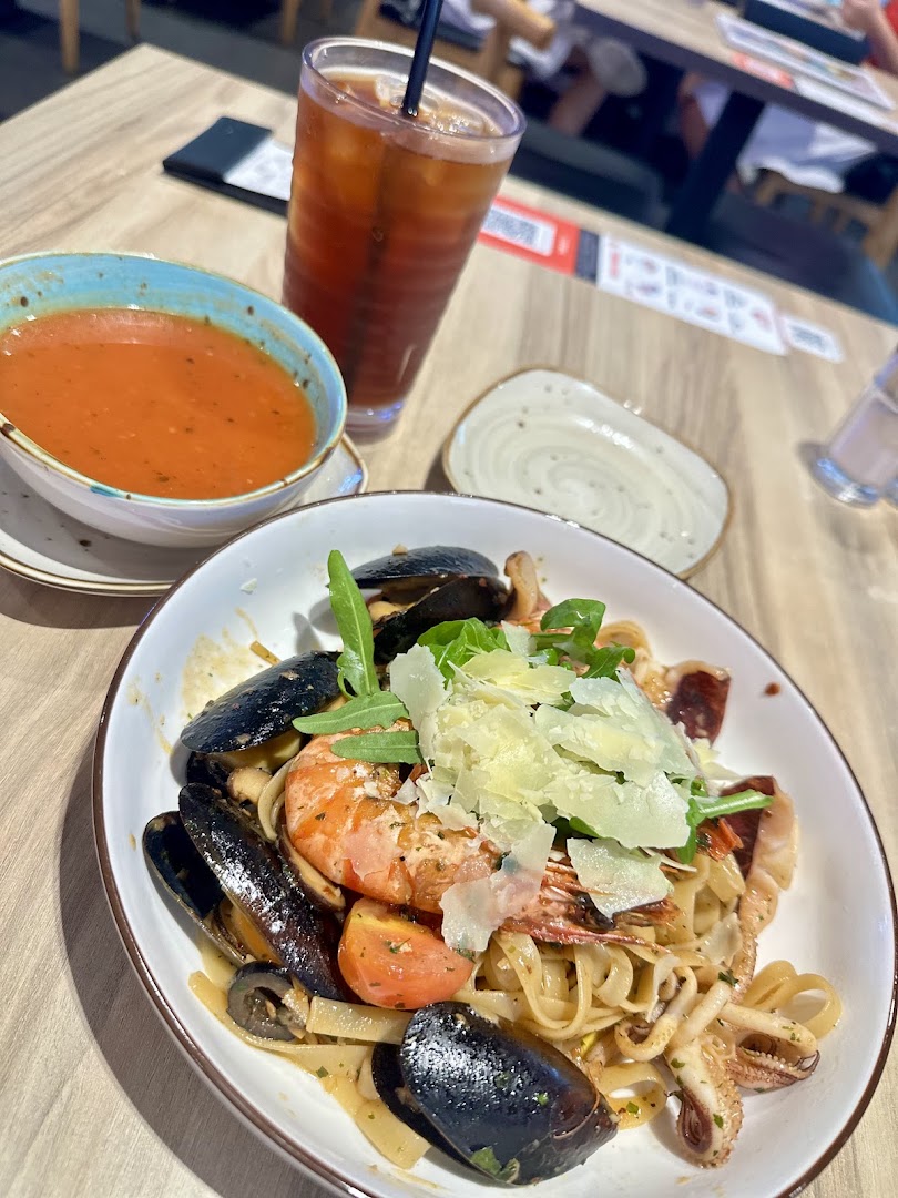 A delicious plate of seafood pasta with mussels, prawns, and squid, served with soup and a drink.
