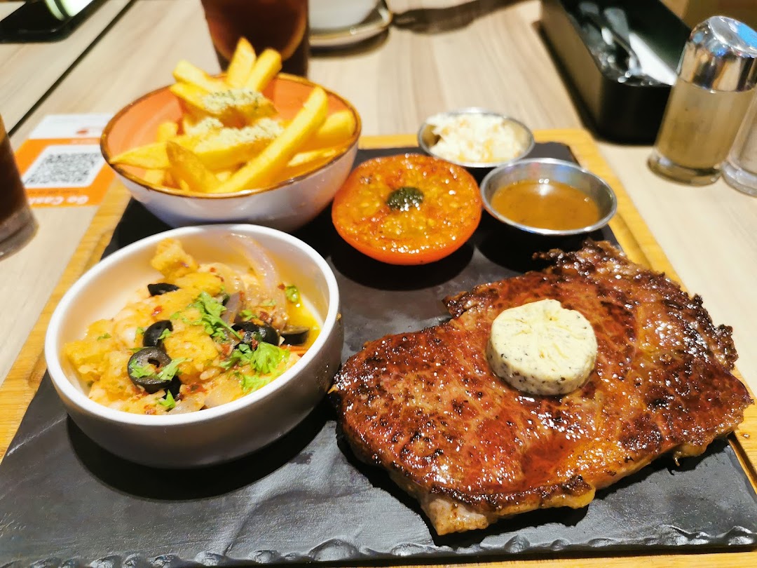 A delicious steak served with fries, a roasted tomato, and a side dish on a wooden board.