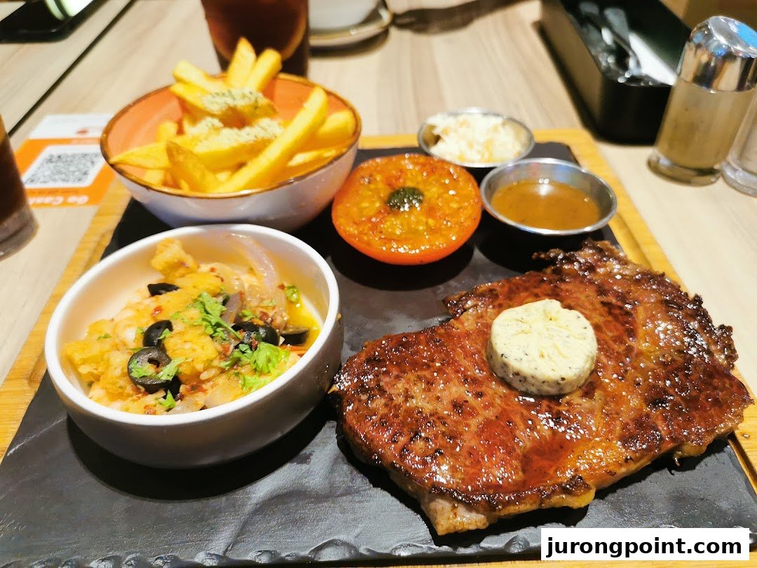 A delicious steak served with fries, a roasted tomato, and a side dish on a wooden board.