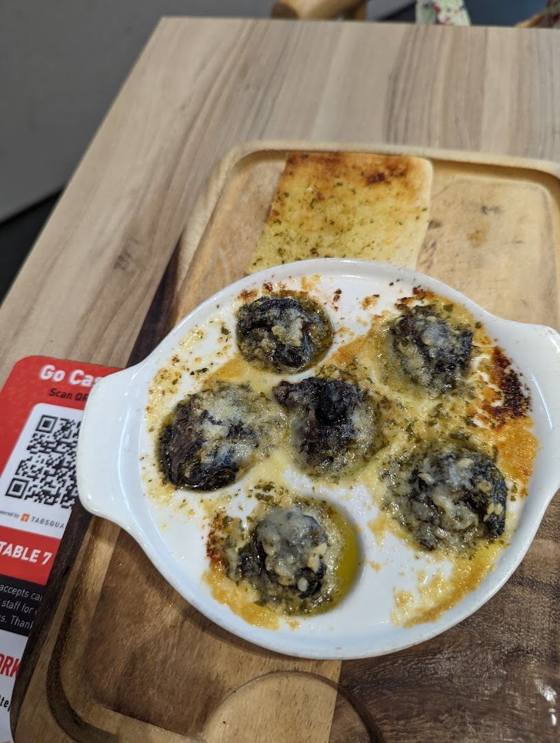 A close-up of baked escargots with garlic bread served on a wooden board at Hot Tomato.