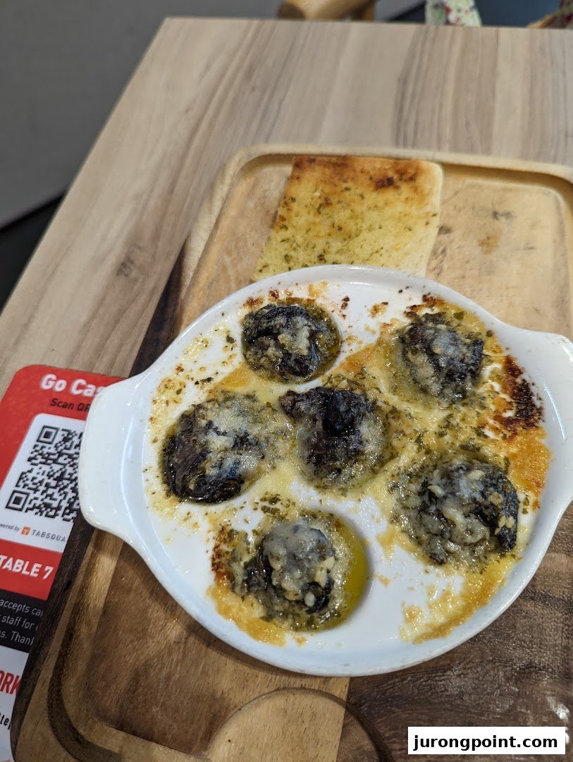A close-up of baked escargots with garlic bread served on a wooden board at Hot Tomato.