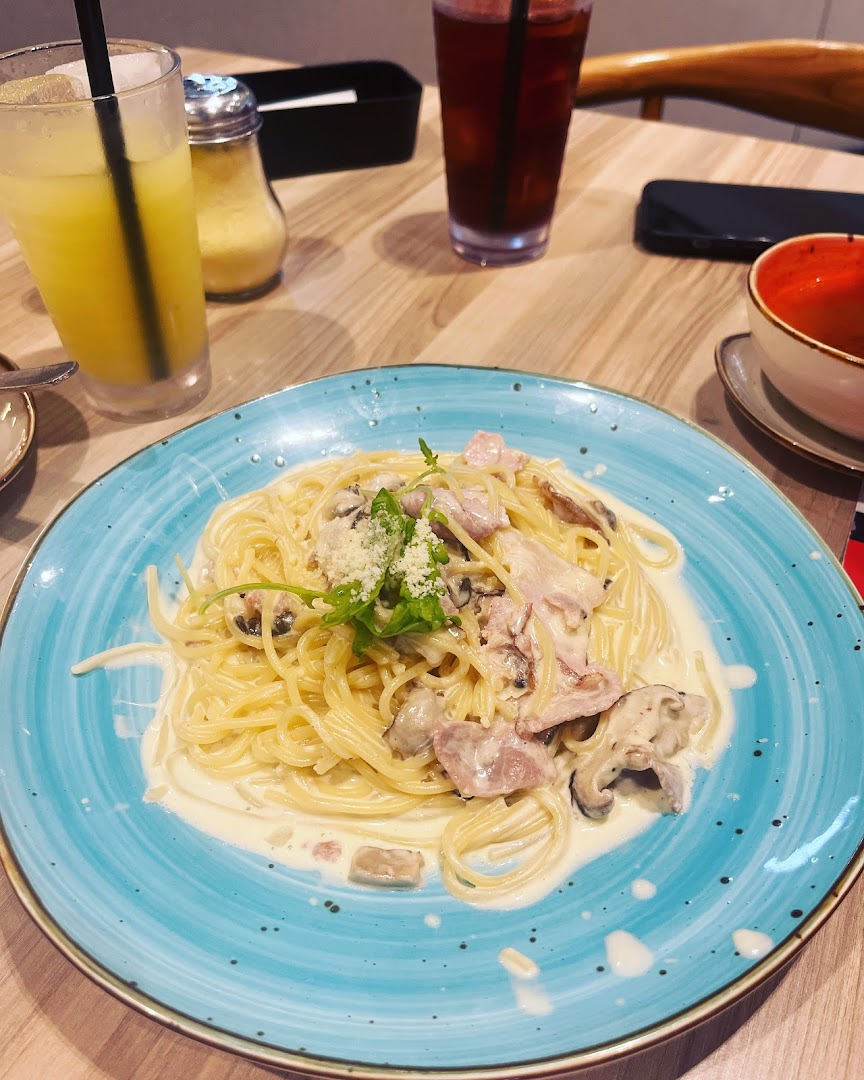 A creamy pasta dish with mushrooms and bacon, served on a blue plate with drinks on a wooden table.