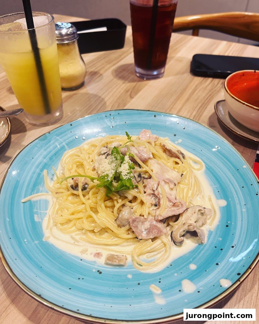 A creamy pasta dish with mushrooms and bacon, served on a blue plate with drinks on a wooden table.