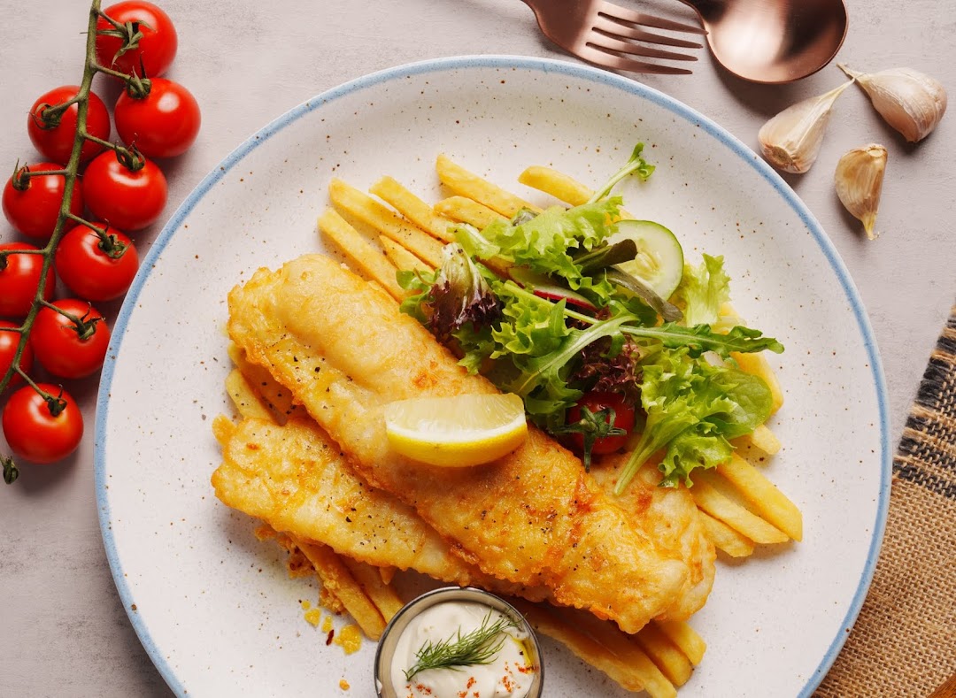 A plate of golden fish and chips with a side salad, lemon, and tartar sauce.