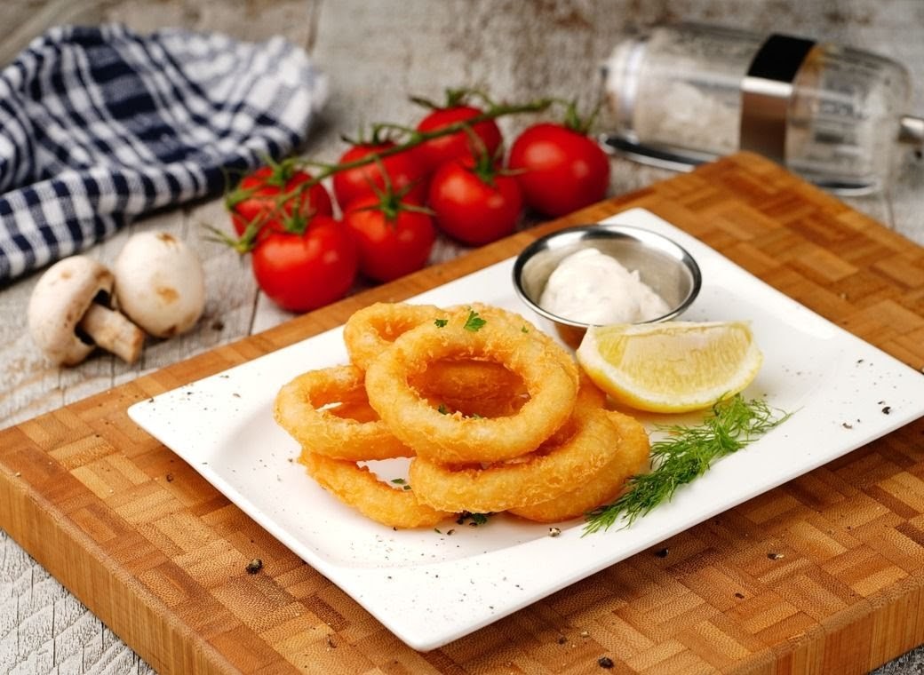A plate of golden fried onion rings with a lemon wedge, dipping sauce, and fresh dill.