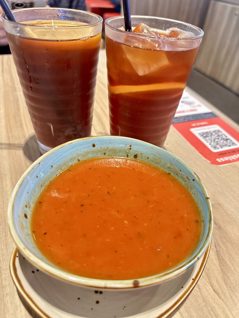 A vibrant bowl of tomato soup with two refreshing iced teas on a wooden table.