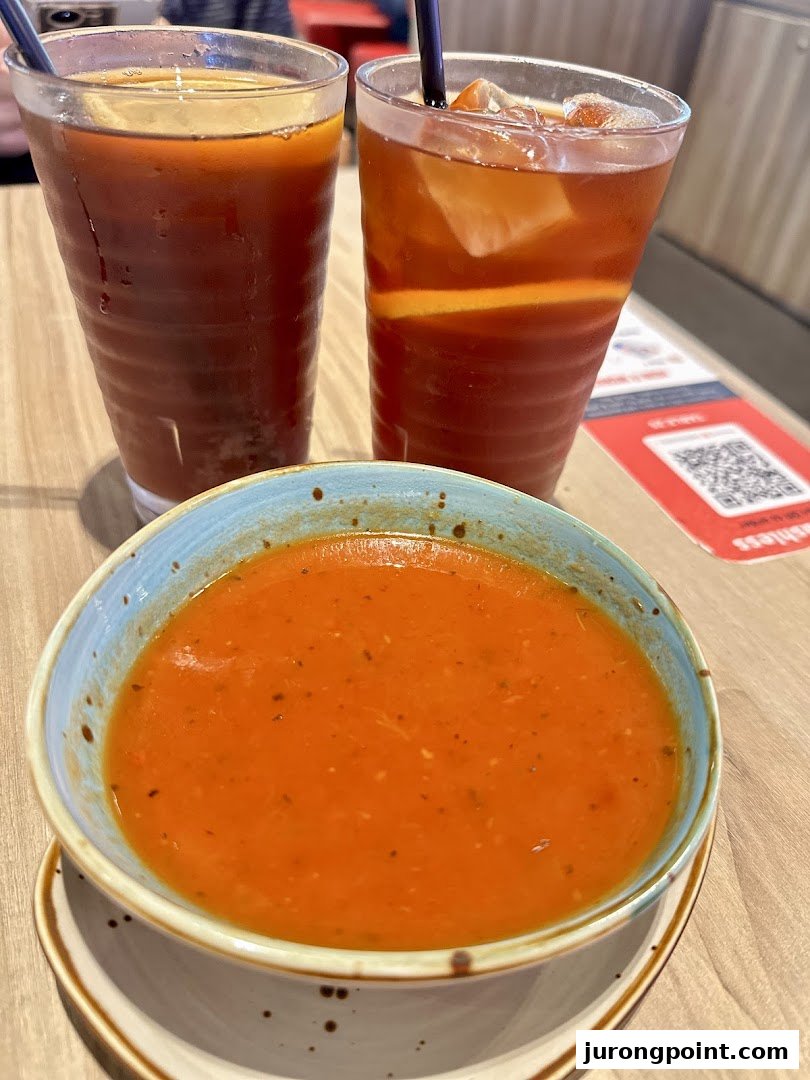 A vibrant bowl of tomato soup with two refreshing iced teas on a wooden table.
