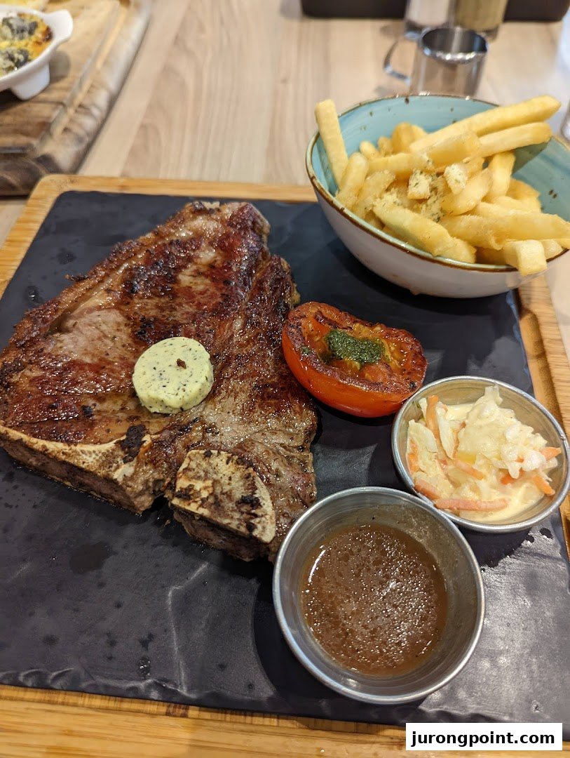 A perfectly grilled T-bone steak served with golden fries, roasted tomato, coleslaw, and sauce.