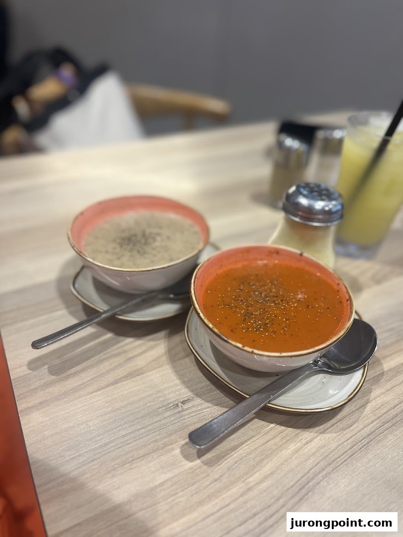 Two bowls of delicious soup, one tomato and one creamy, served on a wooden table.