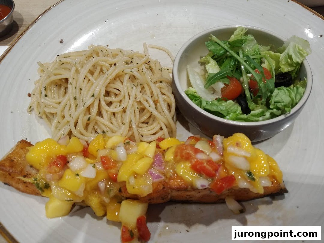 A plate featuring pan-seared fish with mango salsa, spaghetti, and a fresh side salad.