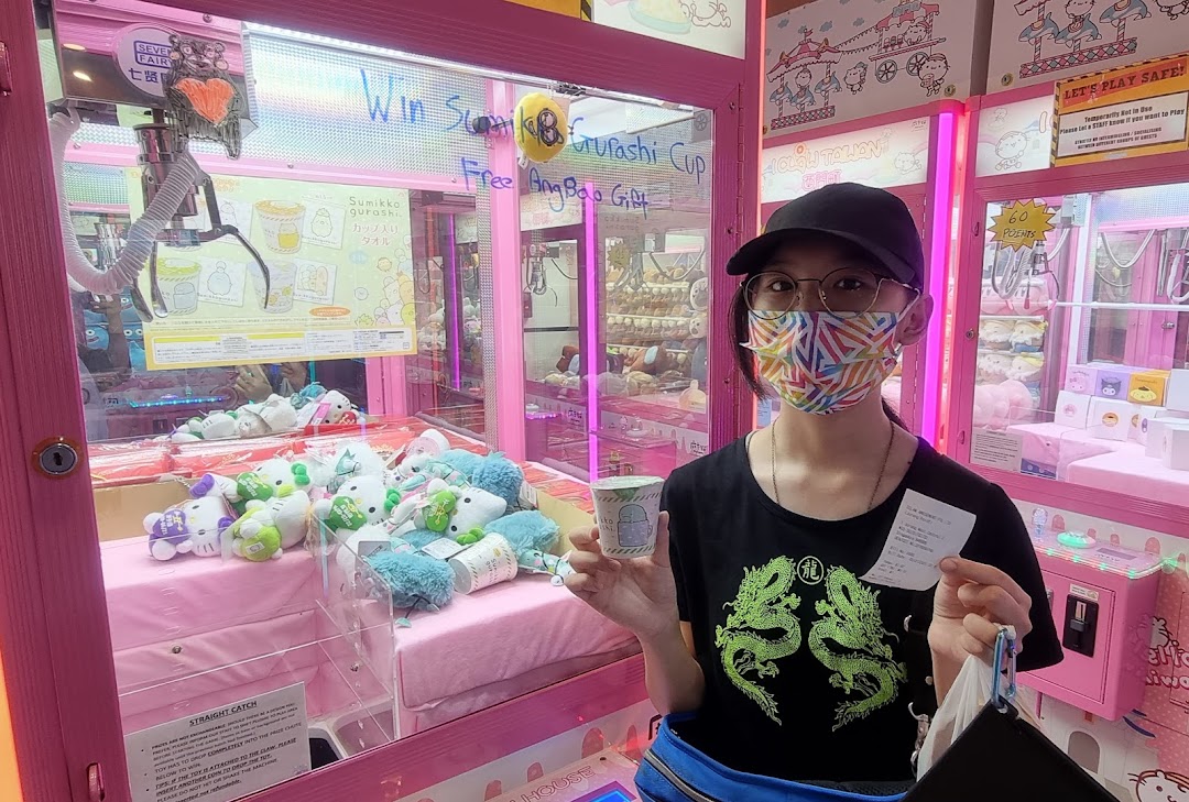 A person holds a prize and receipt in front of pink claw machines filled with plush toys at iClaw Taiwan.