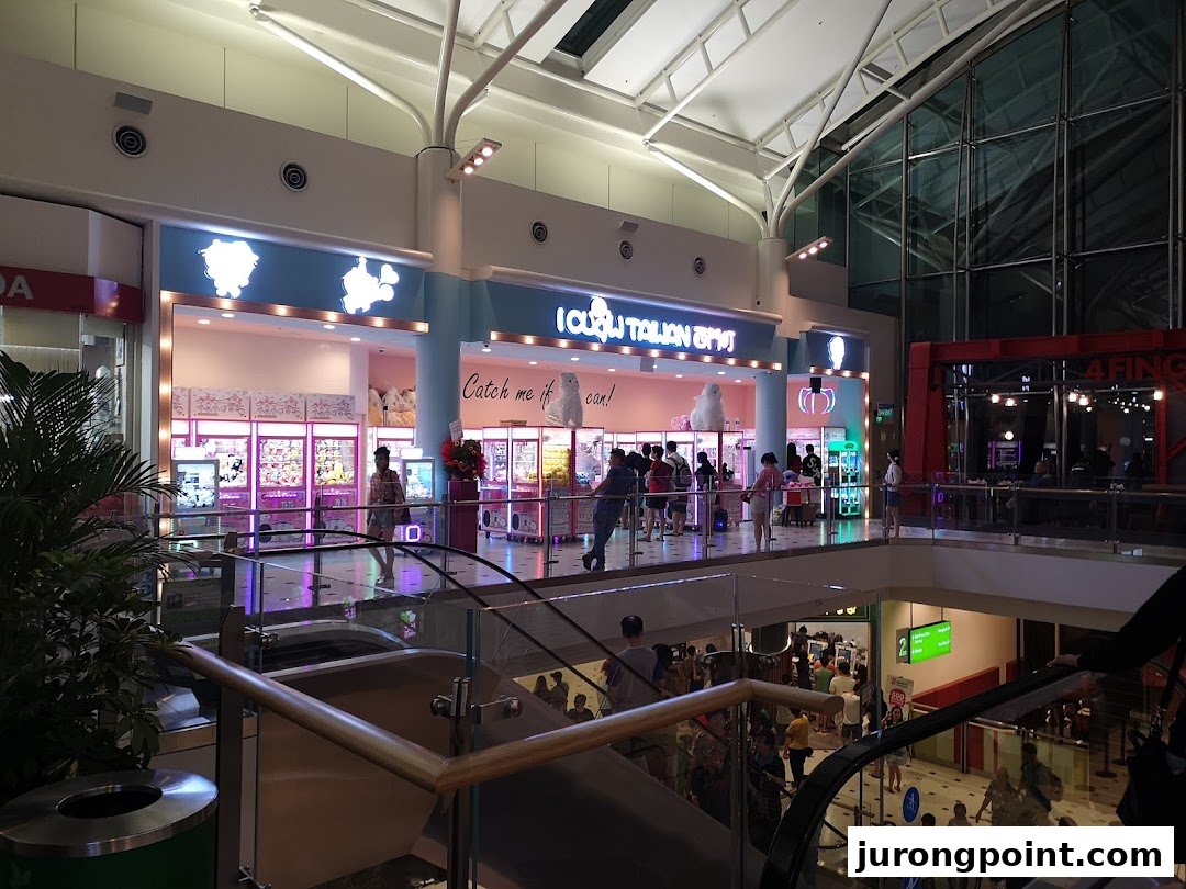 Brightly lit iClaw Taiwan claw machine arcade entrance with people playing, viewed from a mall escalator.