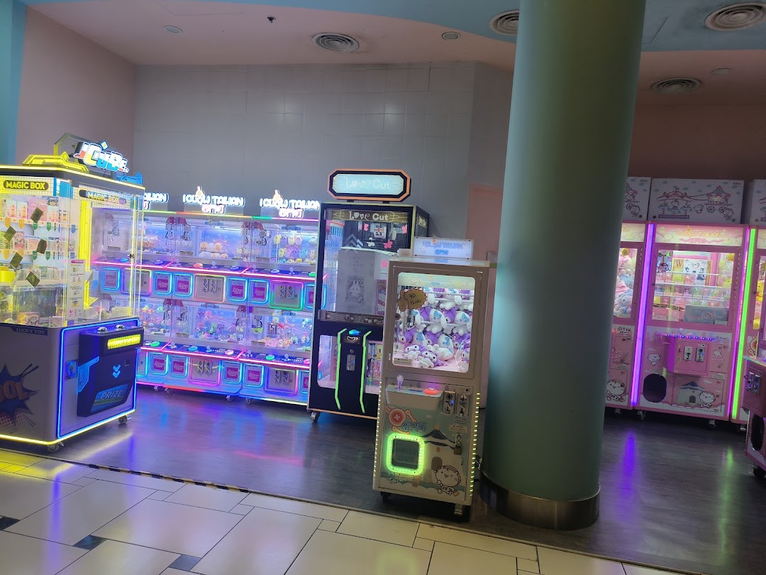Brightly lit arcade interior with numerous claw machines filled with various prizes.