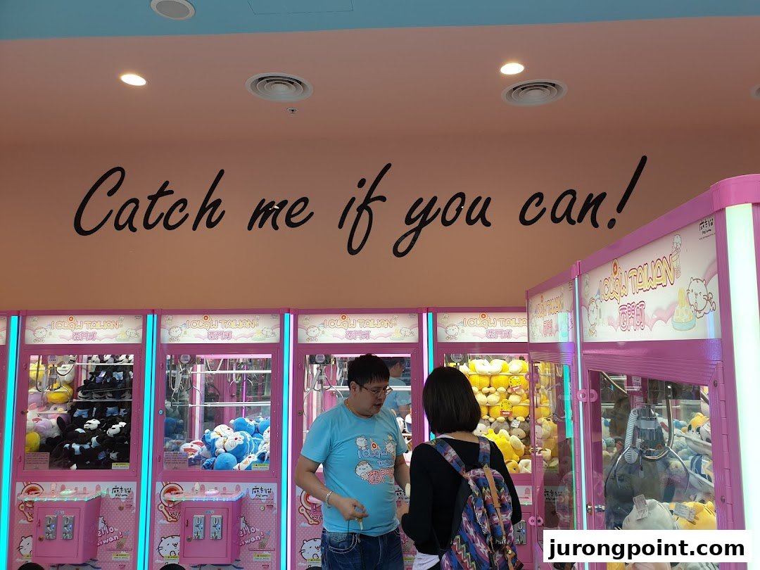 People playing claw machines inside iClaw Taiwan, with a 'Catch me if you can!' slogan on the wall.