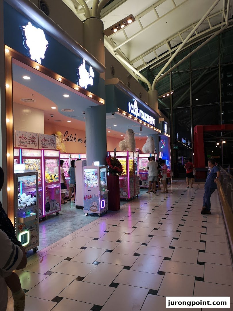 A brightly lit iClaw Taiwan shop entrance with multiple claw machines and people playing.