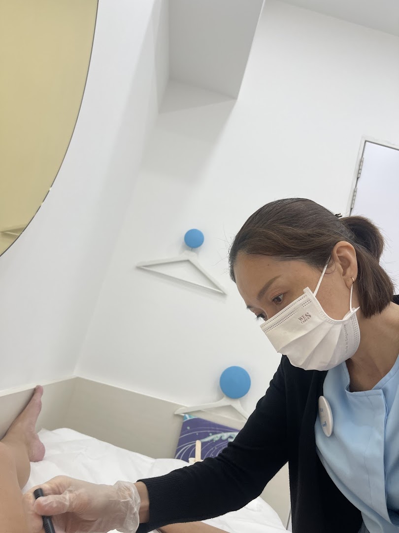 A staff member in a mask and gloves performs a treatment on a client's leg in a clean, bright room.