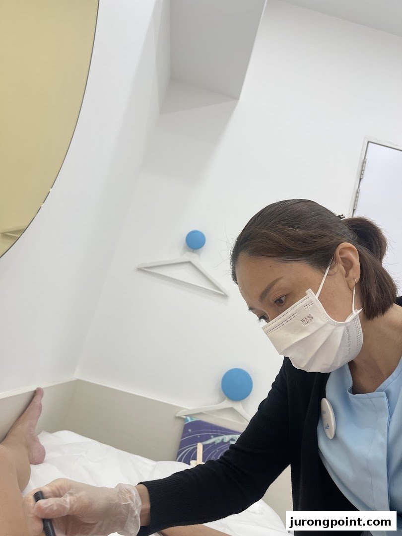 A staff member in a mask and gloves performs a treatment on a client's leg in a clean, bright room.