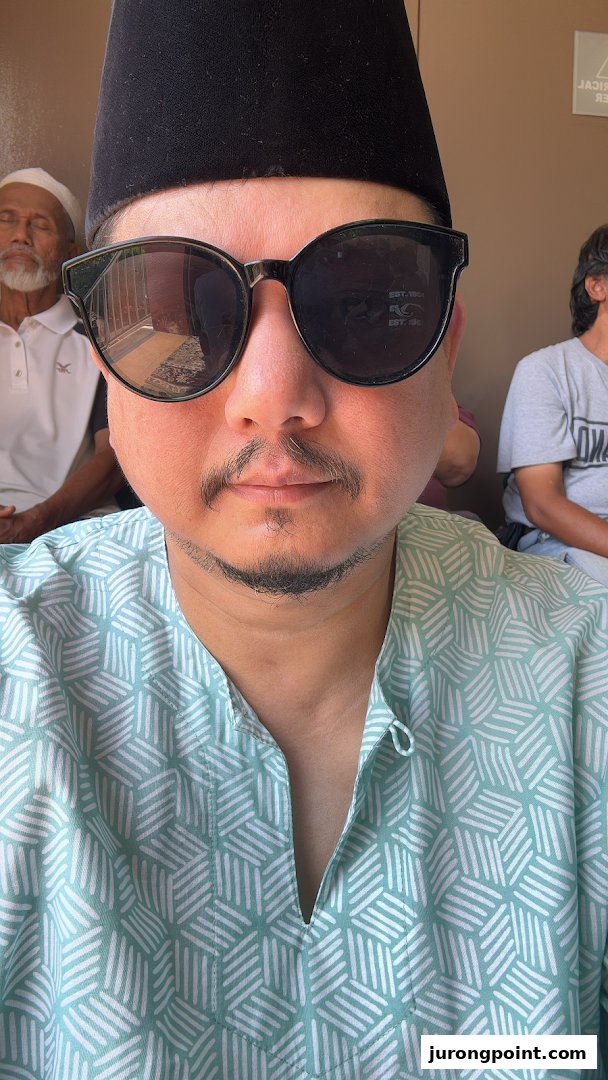 A person wearing sunglasses and a traditional hat, with other individuals in the background.