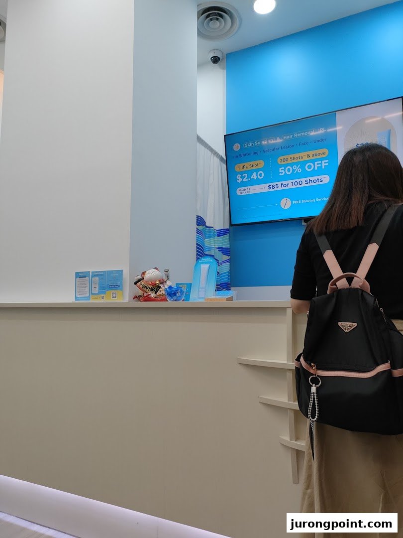 A customer stands at the counter of Japan IPL Express, facing a digital display advertising IPL services.