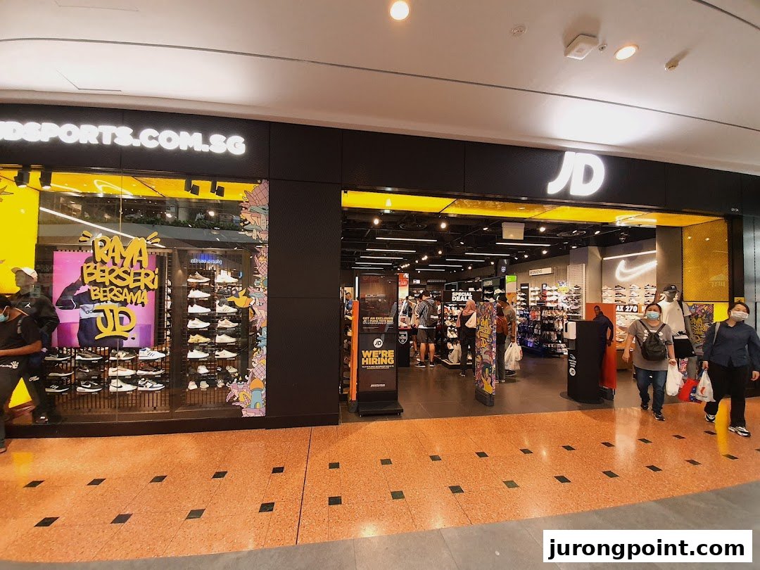 The vibrant storefront of JD Sports, showcasing athletic footwear and apparel, with customers entering and browsing.