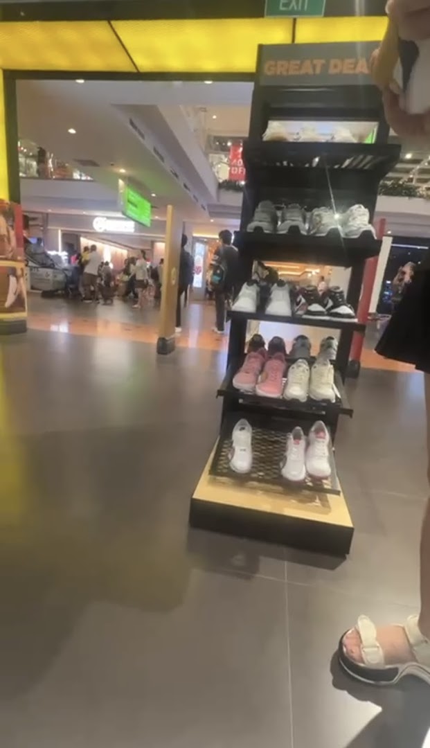 An in-store display showcasing a variety of athletic footwear, with shoppers in the background.