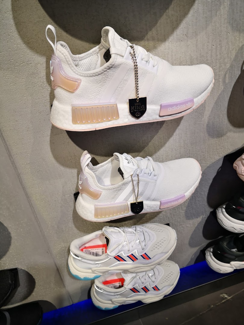 A display of various Adidas sneakers, including white NMDs and other models, showcased in a retail store.