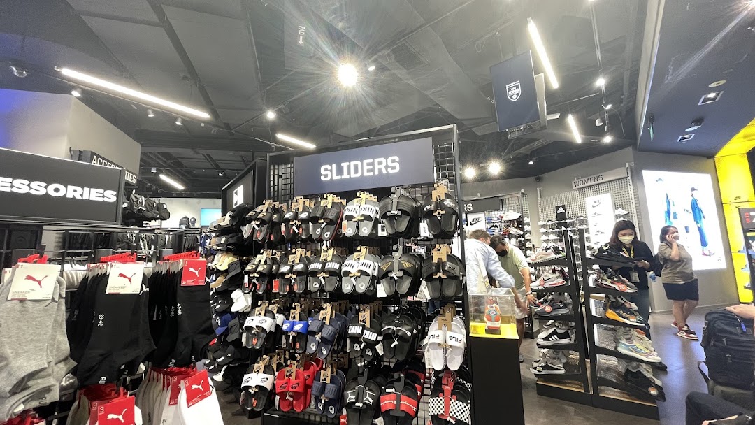 Interior view of JD Sports showcasing a wide range of sliders, socks, and sneakers, with customers browsing.