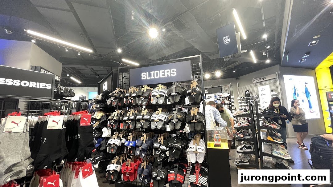 Interior view of JD Sports showcasing a wide range of sliders, socks, and sneakers, with customers browsing.