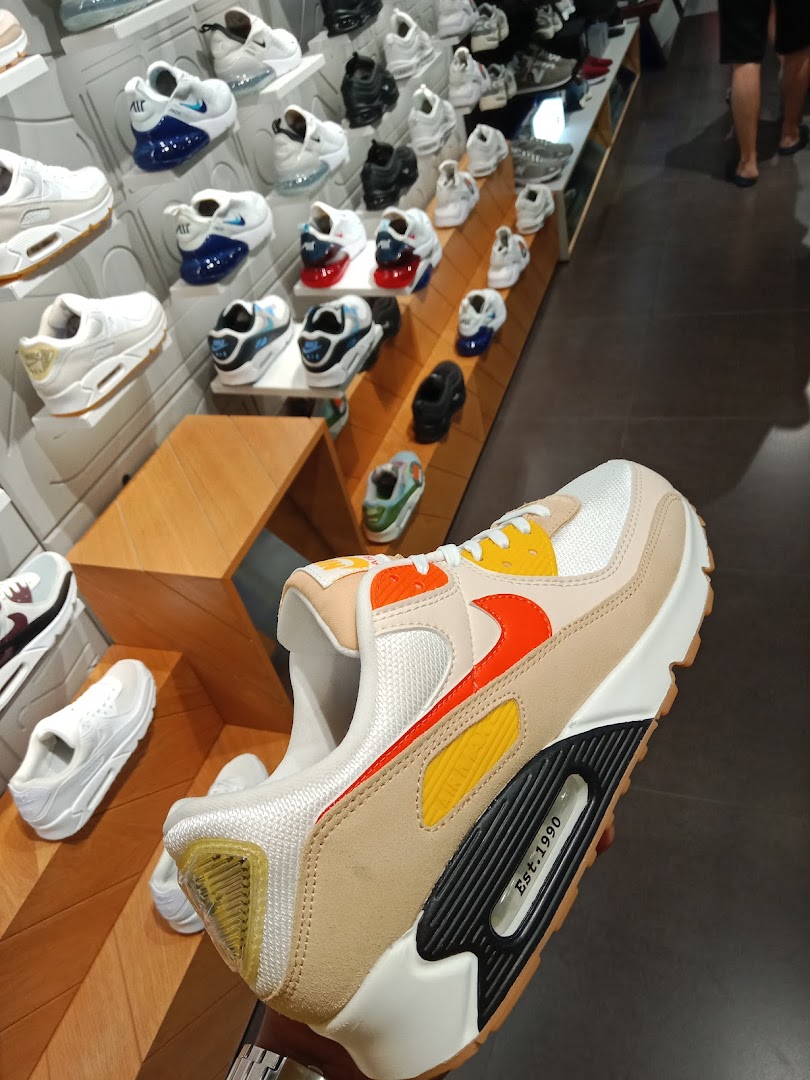 A close-up of a Nike Air Max sneaker held in hand, with various other sneakers displayed in a JD Sports store.