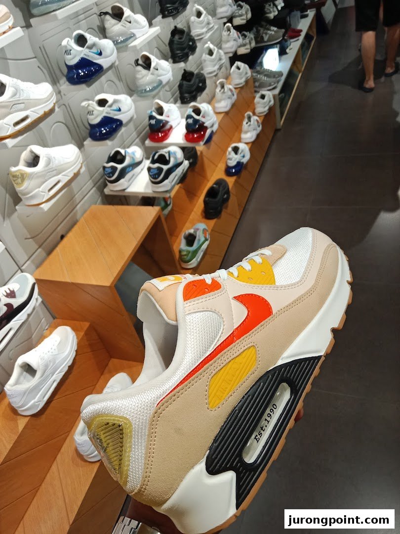 A close-up of a Nike Air Max sneaker held in hand, with various other sneakers displayed in a JD Sports store.