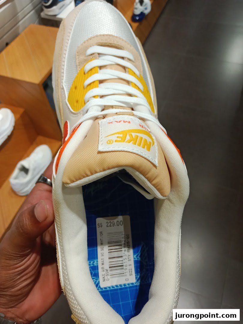 A close-up of a Nike Air Max 90 shoe with a price tag of S$229.00 inside a JD Sports store.