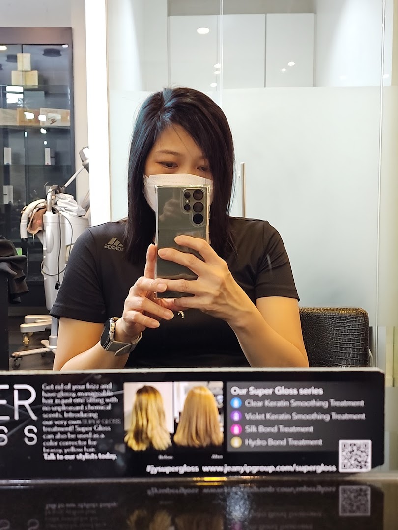 A customer takes a selfie in a Jean Yip Aesthetics salon, featuring a display board for Super Gloss hair treatments.