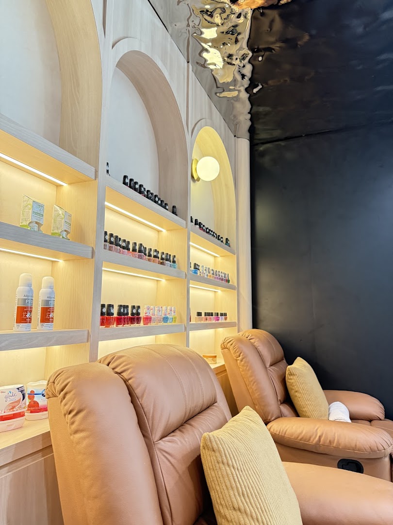 Comfortable recliners and illuminated shelves displaying beauty products, indicating a relaxing spa or nail service area.