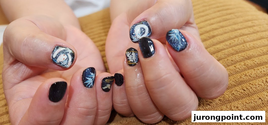 Close-up of hands displaying intricate dark blue and glitter nail art with white, Asian-inspired designs.